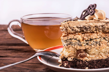 Piece of cake with chocolate and cream on a plate with a cup of herbal tea on a table close-up