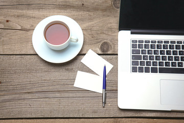Blank business cards with pen, laptop and tea cup on wooden