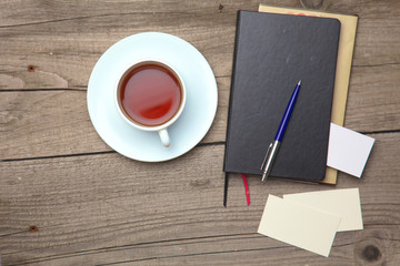 Blank business cards with pen, notebook and tea cup on wooden