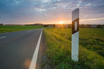 Landstraße mit Leitpfosten und Sonnenuntergang