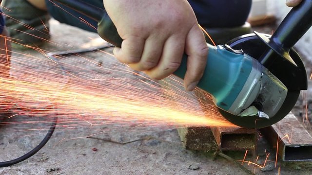 Worker in gloves cutting a steel rail with angle grinder
