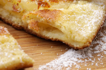 angeschnittener Apfelpfannkuchen mit Puderzucker auf Holzbrett