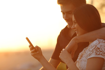 Couple using a smartphone in a sunset back light - Powered by Adobe