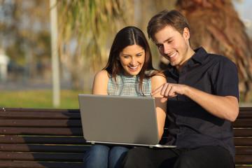 Couple watching media in a laptop sitting on a bench