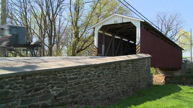 An Amish horse and buggy cart pass through a covered bridge in rural Lancaster, Pennsylvania.