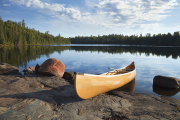 Yellow canoe on rocky shore of calm lake with pine trees