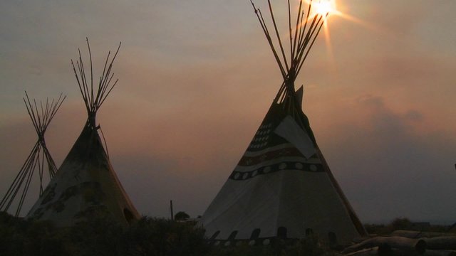 Indian teepees stand in a native american encampment at sunset.