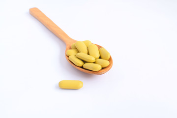 Green pills in wood spoon on white background, selective focus
