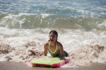 Girl child landing on the sand as she rides the boogie board.