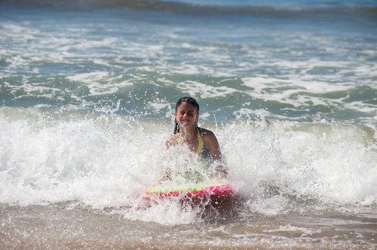 Girl child getting splashed in the face as she rides the boogie board.