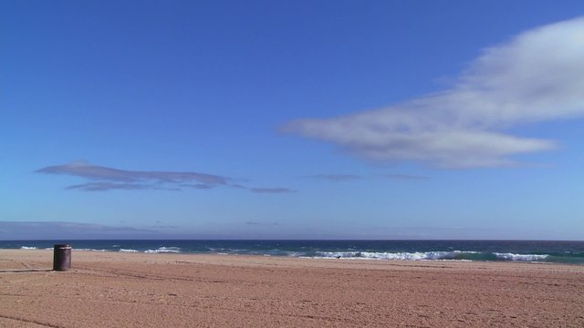 An empty beach with a lone garbage can and blue sky.