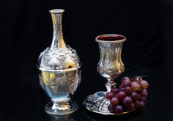 Wine bottle and a glass of pure silver with grapes