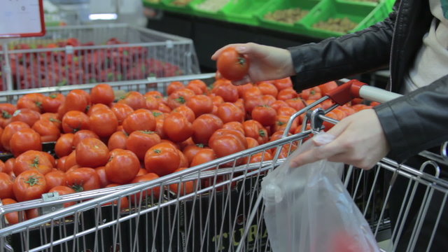 Young woman in supermarket. Buyer picks the tomatoes out of the box