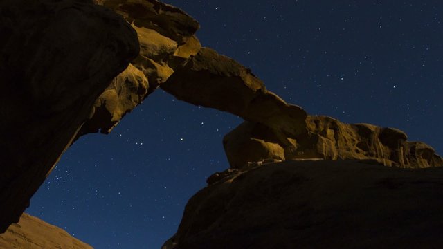 An incredible time lapse shot looking up at an arch formation in the desert against a night sky.