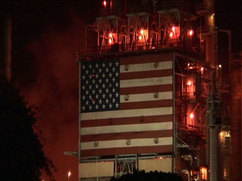 An American flag mural decorates the side of an oil refinery at night.