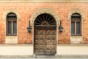 Rustic facade of a building. Double wooden door and windows with arcs.