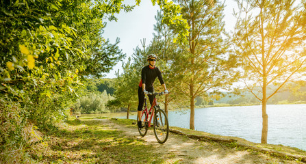 Young woman riding a bike in the forest next to a lake at sunset.