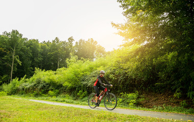 Young biker woman riding a bike in the forest at sunset..
