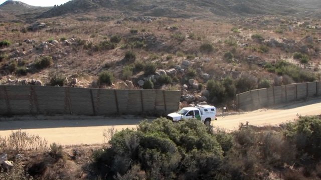 A vehicle travels up a road bordered by a tall fence.