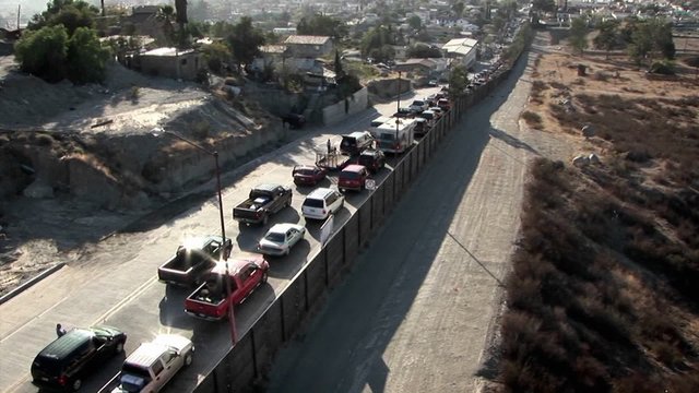 Cars are lined up in two rows along a tall fence.