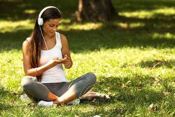 Beautiful Young Woman with Headphones sitting on grass and listening to music