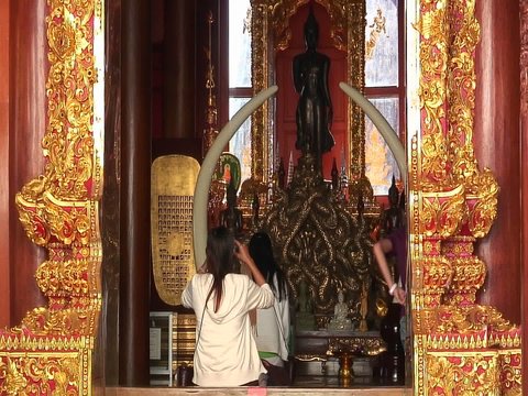 A young woman enters a Buddhist temple and sits to and begins to pray.