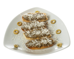 Four bruschetti with olives pate and grated cheese served on a white plate. Isolated on white.