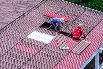 Man workers replacing damaged old tiles roof.