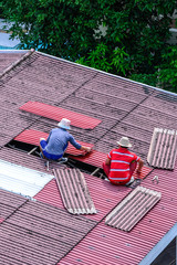 Man workers replacing damaged old tiles roof.
