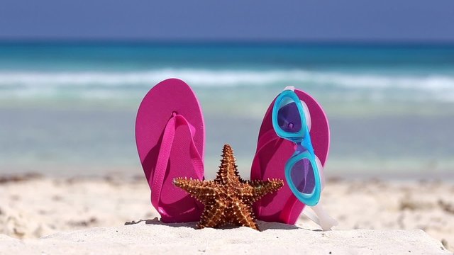 Pink flip flops, swimming glasses and starfish on white sandy beach. Summer vacation concept