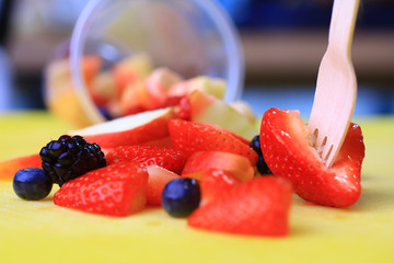fruit cup tilted and fruits spilled and scattered with a wooden fork