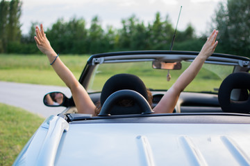 Beautiful young woman in convertible with hands up.Interior is black-blue color, with upholstery in the same color. In the background is forest. Focus on the handle behind her head.