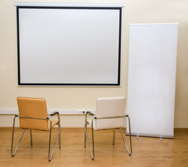 Blank white screen and roll-up banner and two chairs