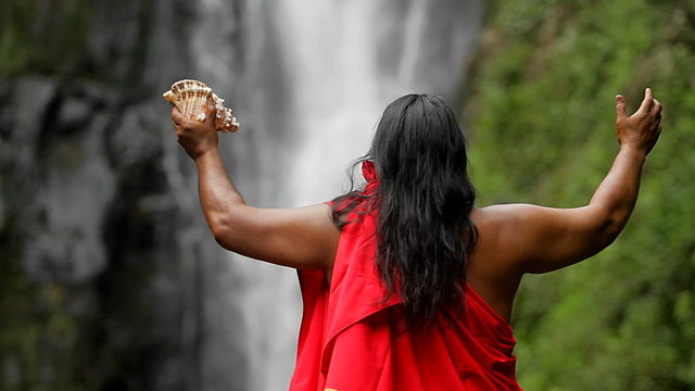 A Hawaii native holds out his hands to bless a waterfall.