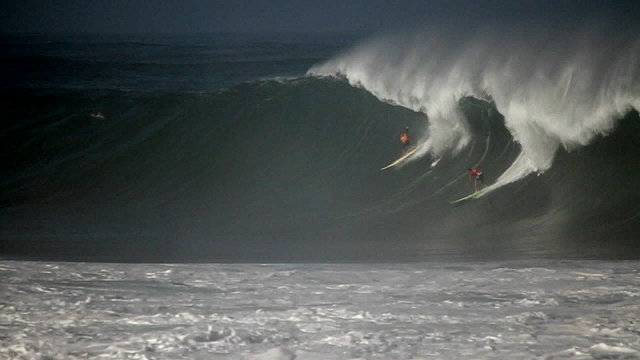 Multiple surfers ride very big waves in Hawaii.
