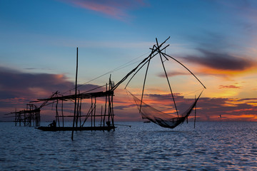 A Silhouette Fisherman Catching Fish from square dip net at Pak Pra Canal in early morning during golden sunrise moment