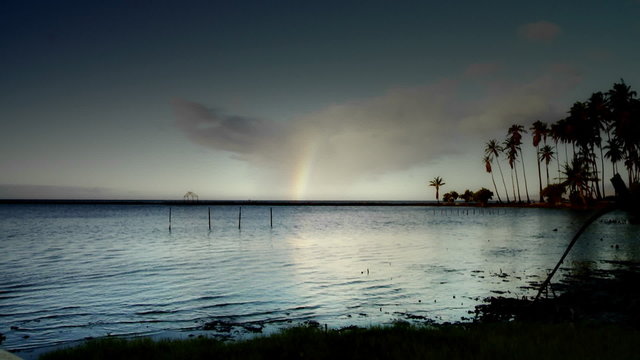 A time lapse show of clouds over a Hawaiian scene, with a rainbow forming.
