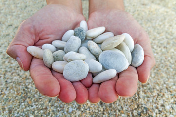 Woman hands holding small stones in hands on beach background