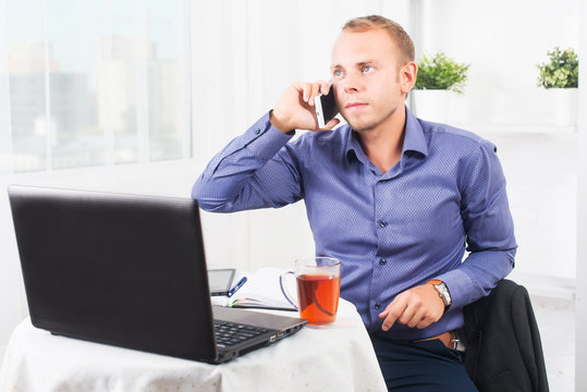 Young businessman working in office, sitting at a table and talking on the phone.