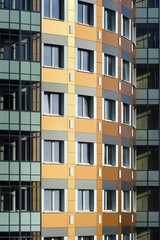 Windows of apartment blocks, residential building in modern architectural style, custom curved orange wall with white and grey construction tile and glazed balconies in green and turquoise shades 