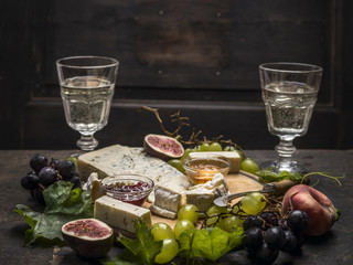Gorgonzola Camembert on a wooden cutting board with a knife for cheese with honey and jam light grape on dark wooden background close up
