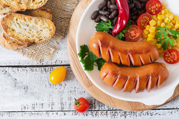 Sausages on the grill with vegetables on a platter. Top view