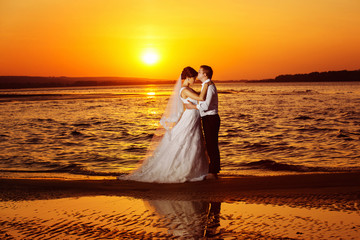 Beautiful wedding couple is kissing at golden tropical sunrise