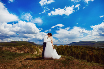 Happy beautiful bride and groom are kissing at top of hill 