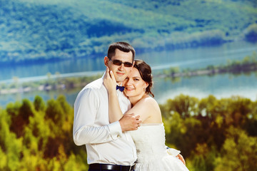 Happy beautiful wedding couple is tenderly huging at top of hill