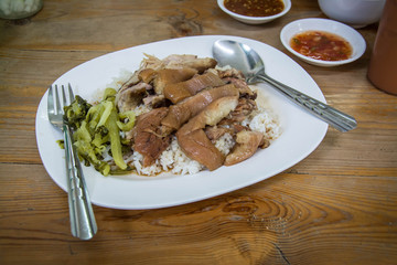 Stewed pork leg on rice with side bowl on wooden table.Thai food