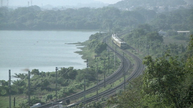An approaching train travels a rural route near a lake.