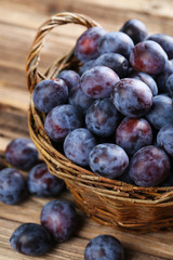Fototapeta premium Fresh plums in basket on the brown wooden background