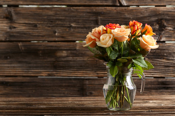 Bouquet of orange roses in vase on brown wooden background