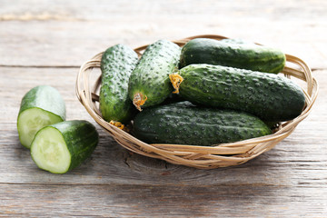 Fresh cucumbers in basket on grey wooden background